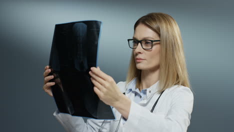 Young-caucasian-attractive-woman-doctor-holding-X-ray-copy-and-studying-it-carefully-on-the-grey-background.-Close-up.